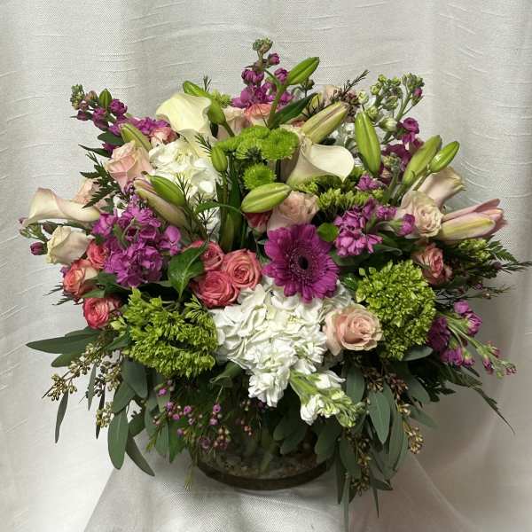 Lush low arrangement of pink roses, white hydrangeas, lilies and bright purple blooms in a clear glass bowl vase