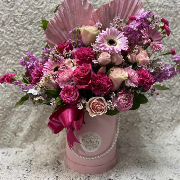 Pink and purple mixed flower arrangement in a pink hatbox with ribbon