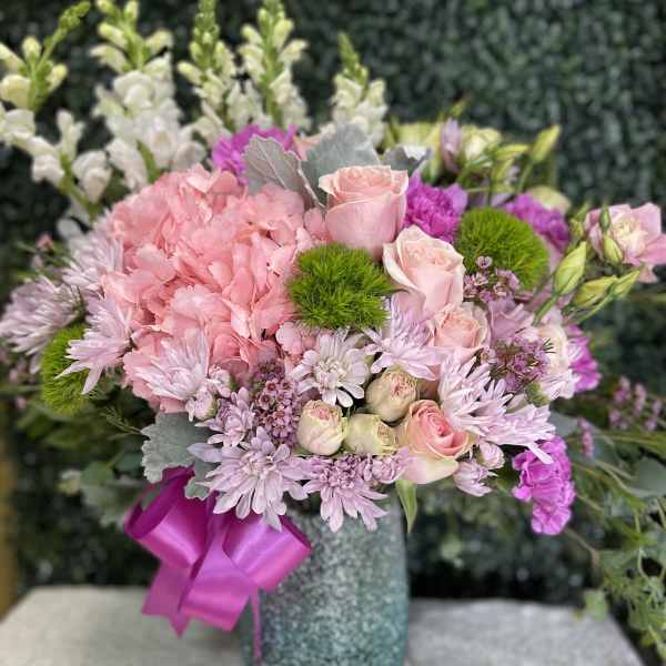 Pink and lavender bouquet in a textured vase with a magenta ribbon