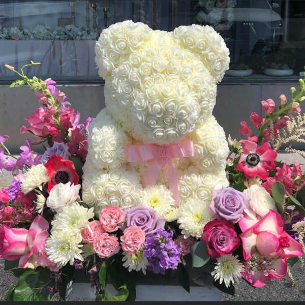 White rose teddy bear surrounded by pink and purple flowers