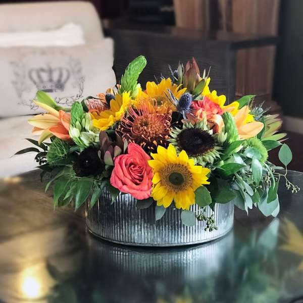 Mixed bouquet of sunflowers, roses, and tropical blooms in a metal container
