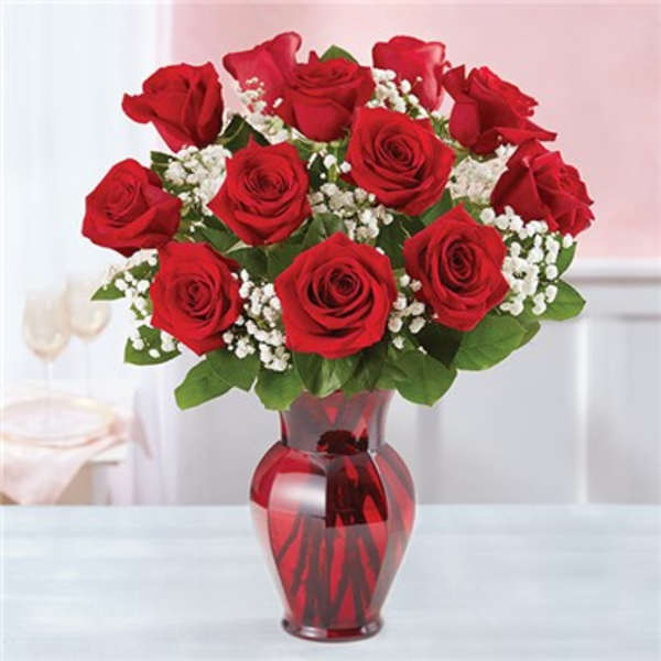 Red roses arranged in a red glass vase with white filler flowers