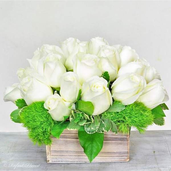 White roses arranged in a wooden box with bright green accents.