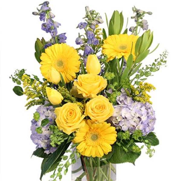 Yellow roses and gerbera daisies with purple flowers in a glass vase