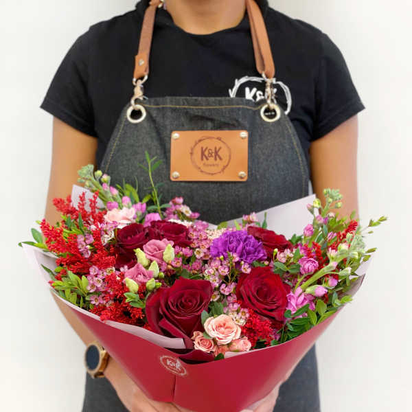 Handheld bouquet of red, pink, and purple roses with mixed filler flowers