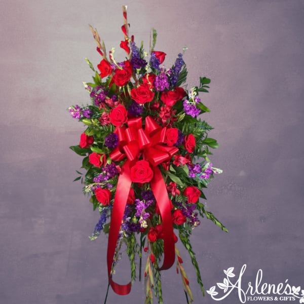 Standing spray of red roses and purple flowers with a large red bow on an easel