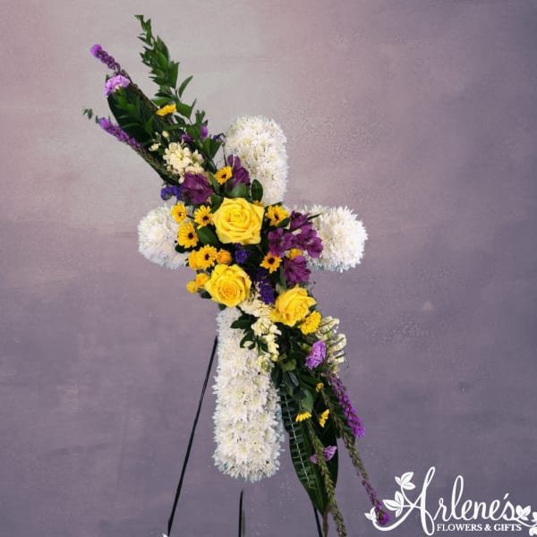 Standing white floral cross with yellow roses and purple flowers on an easel