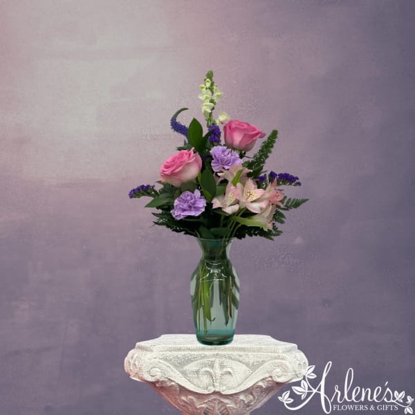 Pink roses and purple flowers arranged in a glass vase