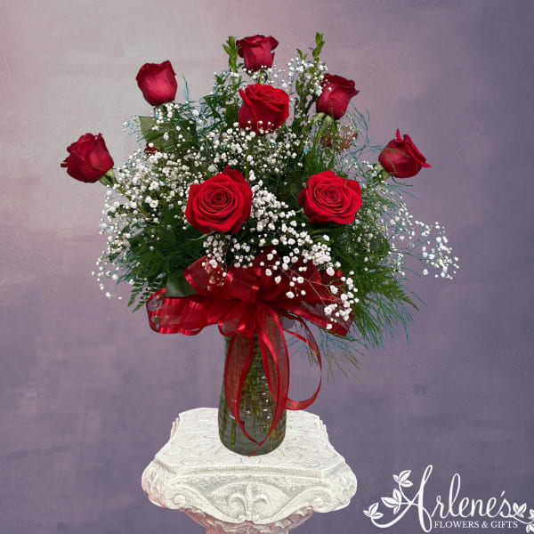 Red roses in a glass vase with baby's breath and a red ribbon
