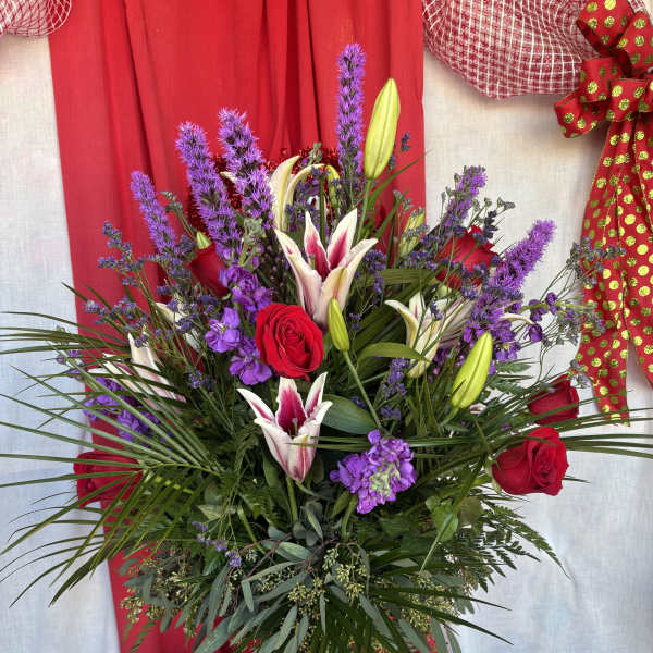 Tall bouquet of red roses, purple flowers, and white lilies in a glass vase