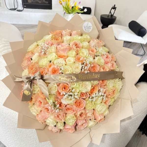 Large bouquet of peach and cream roses wrapped in tan paper with a birthday ribbon