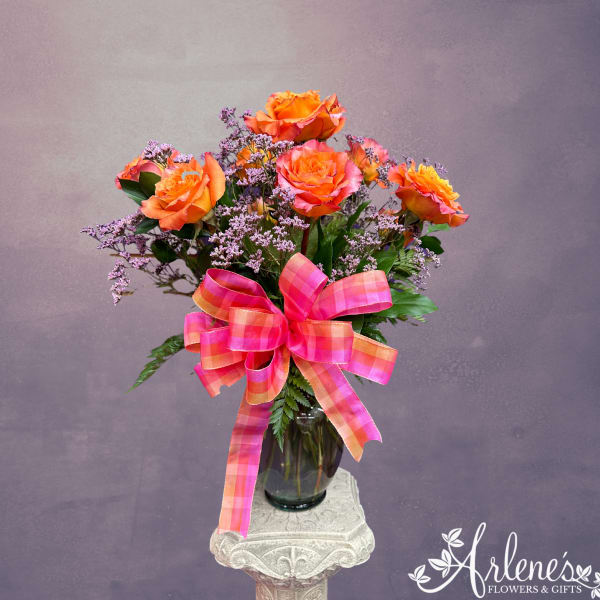Orange roses in a glass vase with a pink plaid ribbon