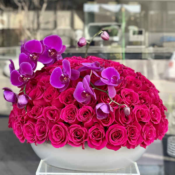 Hot pink roses with purple orchids in a white bowl vase