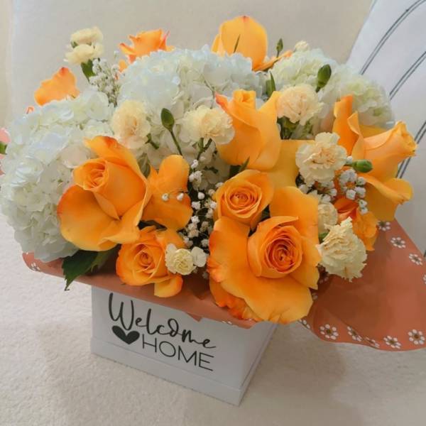 Orange roses and white hydrangeas in a gift box with "Welcome Home" text