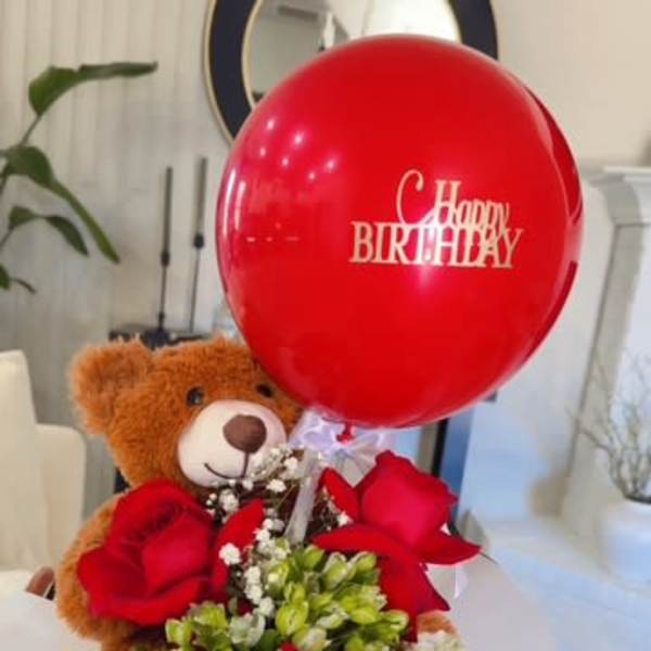 Teddy bear holding red roses with a birthday balloon