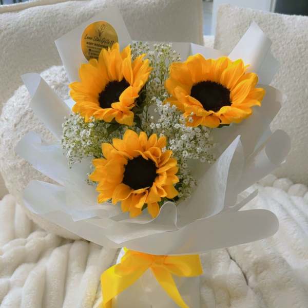 Bouquet of three sunflowers wrapped in white paper with a yellow ribbon