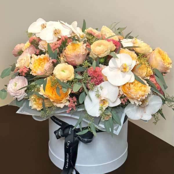 Pastel flower arrangement in a round white box with orchids and roses