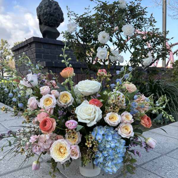 Large mixed bouquet of roses, hydrangea, and tulips in a white container