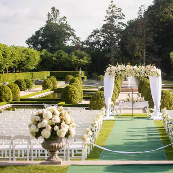 Outdoor wedding aisle with white chairs and floral arch