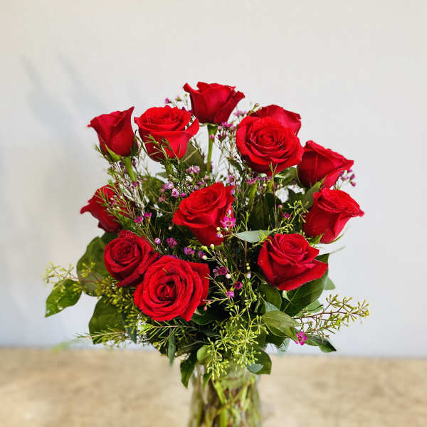 Red roses arranged in a clear glass vase with small pink filler flowers