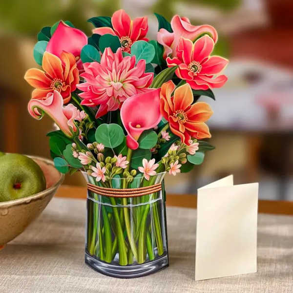 Paper pop-up bouquet of pink and orange flowers in a vase with a blank cream card beside it
