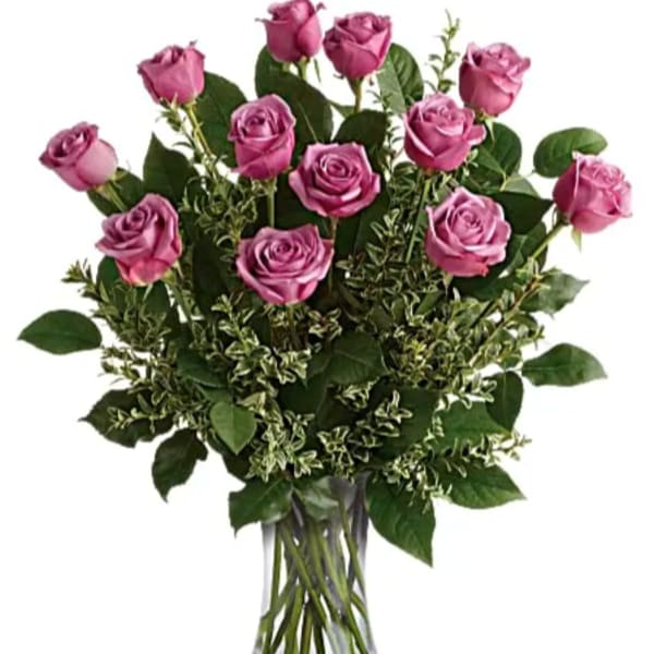 Dozen lavender roses in a clear glass vase with abundant filler foliage