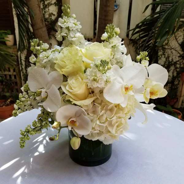 White floral arrangement in a dark vase with orchids and roses
