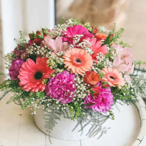 Round arrangement of pink and peach flowers in a low white container