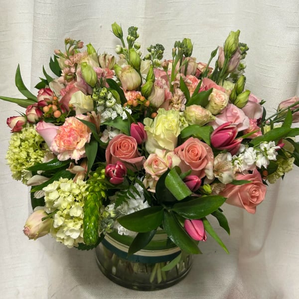 Low glass vase of pink and cream roses, tulips, carnations, and hydrangeas in a lush mixed arrangement