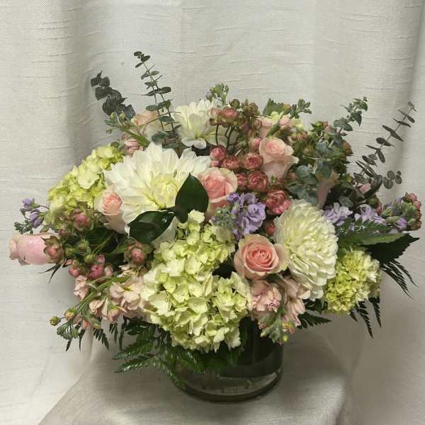 Pastel arrangement of pink roses, white mums, and green hydrangeas in a clear glass vase.