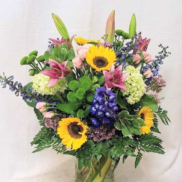 Mixed arrangement with sunflowers, lilies, roses, hydrangeas and delphinium in a glass vase