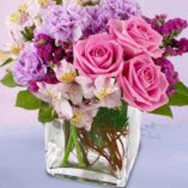 Pink roses and purple flowers arranged in a clear square vase