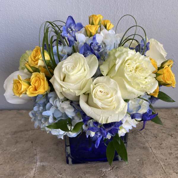 Blue and white floral arrangement with yellow roses in a cobalt vase