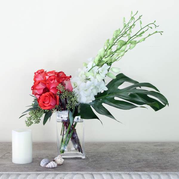 Red roses and white orchids in a clear vase with large tropical leaves