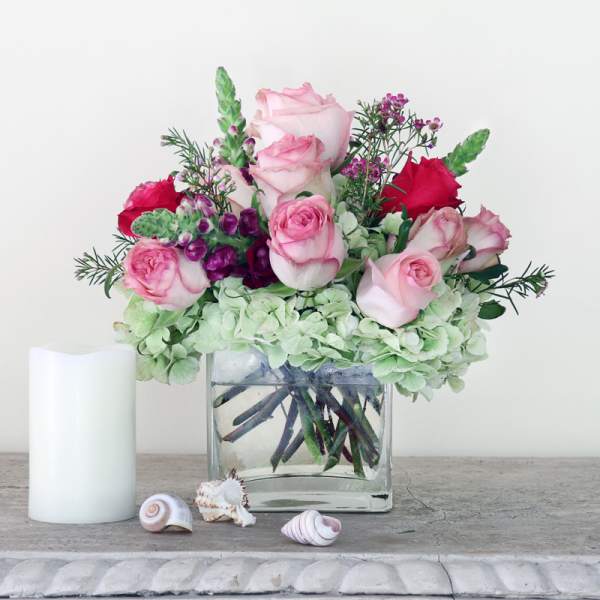 Pink and red roses in a clear glass vase with pale green hydrangeas