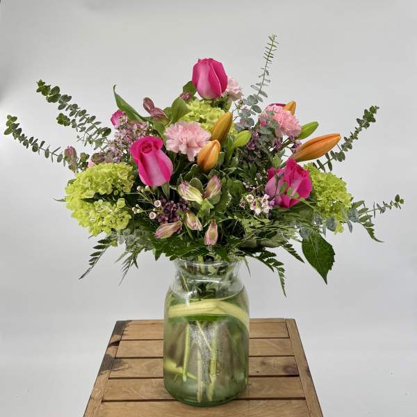 Mixed bouquet of pink roses, orange lilies, and green hydrangeas in a clear glass jar vase