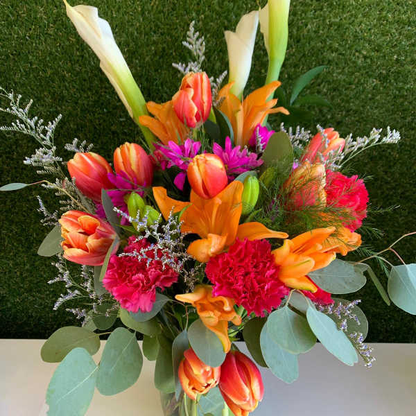 Bright mixed bouquet with calla lilies, tulips, carnations, and lilies in a glass vase