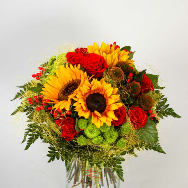 Bright bouquet with sunflowers, red roses, and green mums in a clear glass vase