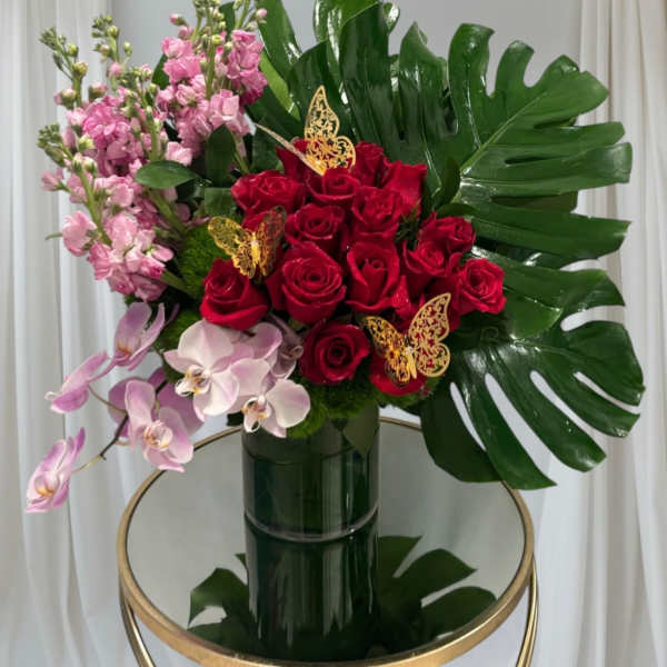 Bouquet of red roses, pink orchids, and pink stock in a dark vase