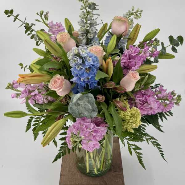 Mixed bouquet in a glass vase with pink roses, lilies, and blue hydrangeas