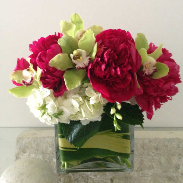 Bouquet of red peonies, white hydrangeas, and green orchids in a glass vase