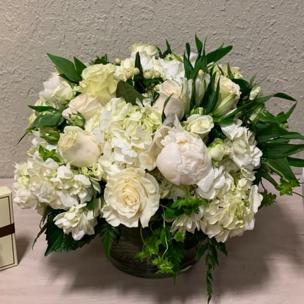 Low round arrangement of white roses, hydrangeas, and peonies in a glass vase