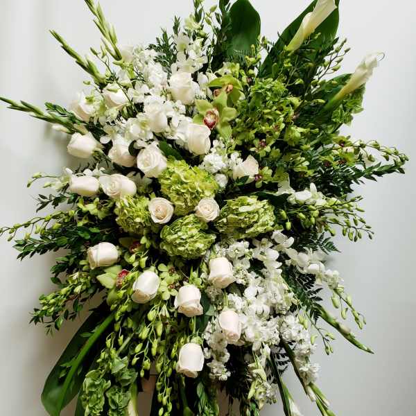 Large white and green funeral spray with roses and orchids on a stand