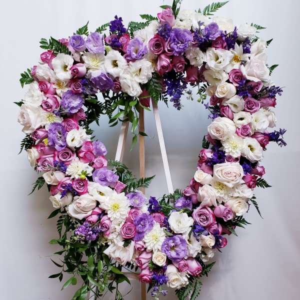 Heart-shaped floral wreath with pink, white, and purple blooms on a stand