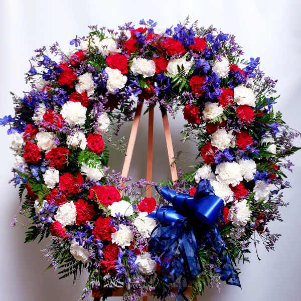 Large red, white, and blue floral wreath on an easel with a ribbon bow