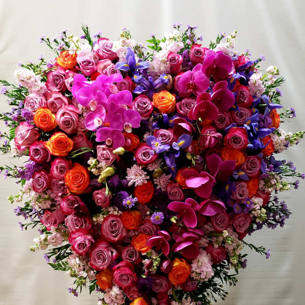 Heart-shaped floral arrangement with pink roses, orchids, and purple flowers