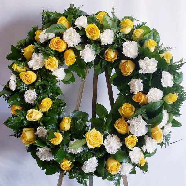Yellow roses and white carnations arranged in a circular wreath on an easel