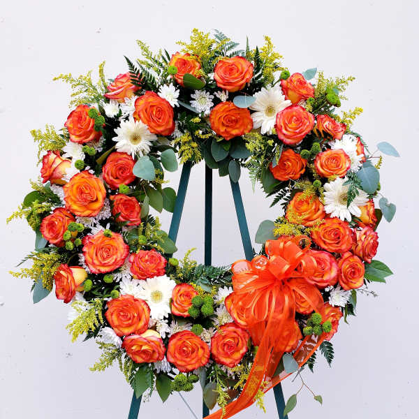 Heart-shaped wreath of orange roses and white daisies with an orange ribbon