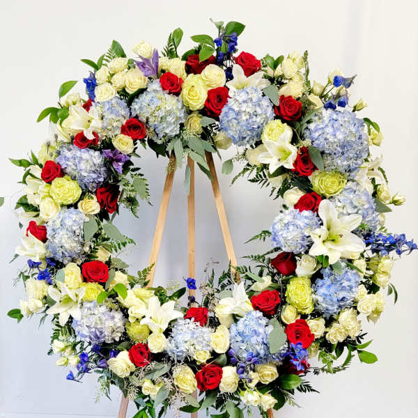 Large floral wreath of red, white, blue, and pale yellow flowers on a wooden stand