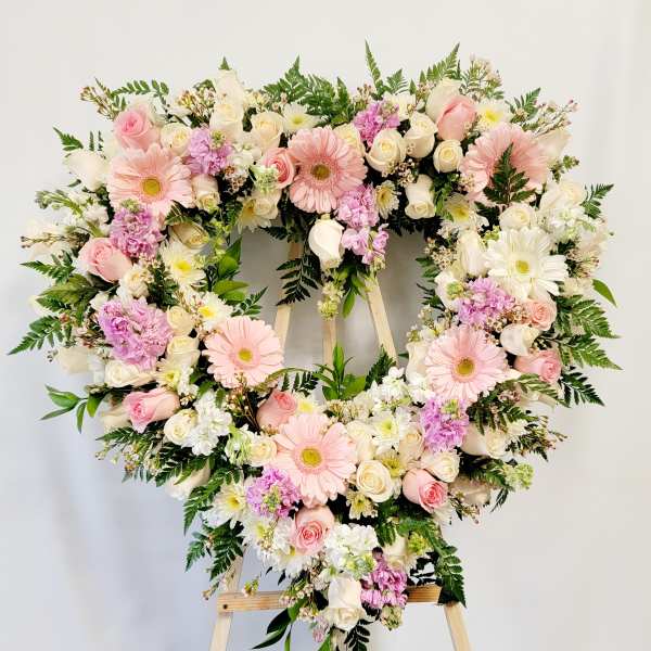 Heart-shaped floral wreath with pink and white flowers on an easel